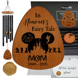 Personalized wooden memorial wind chime set with a large teardrop-shaped wooden plaque engraved with 'In Heaven's Fairy Tale MOM 1949 - 2025' and a black silhouette of a fairy tale castle, shown alongside matching wind chimes, a gold-toned keepsake box, and a gift note on a white background.