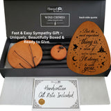 A memorial wind chime gift set shown in an open black presentation box with a handwritten gift note included. The set includes a large round wooden wind chime, a smaller round wooden wind chime, a single wooden chime with a string, and a black metal wind chime.