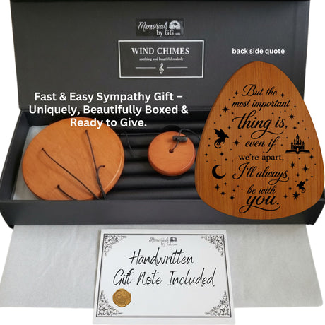 A memorial wind chime gift set shown in an open black presentation box with a handwritten gift note included. The set includes a large round wooden wind chime, a smaller round wooden wind chime, a single wooden chime with a string, and a black metal wind chime.